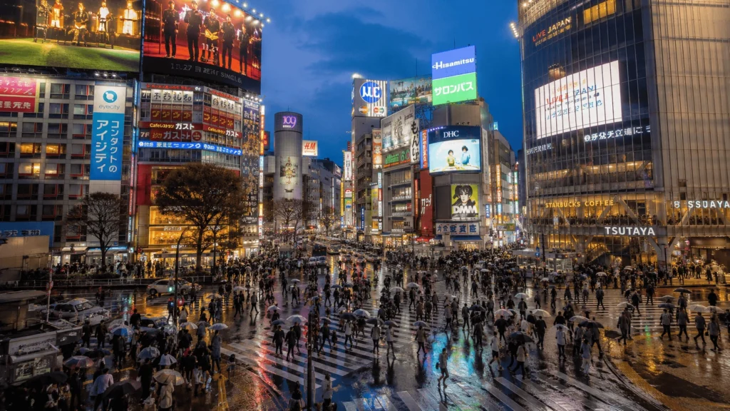 Shibuya Crossing in Tokyo at dusk with neon signs reflected on wet pavement